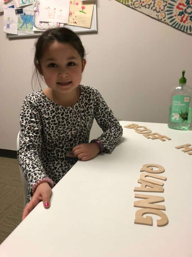 A little girl sitting at a table with letters on it.